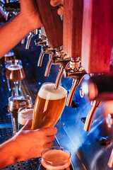 Fototapeta na wymiar Hand of bartender pouring a large lager beer in tap. Bright and modern neon light, males hands. Pouring beer for client. Side view of young bartender pouring beer while standing at the bar counter.