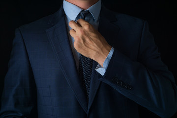 Young man in a blue suit straightens his tie on a dark background