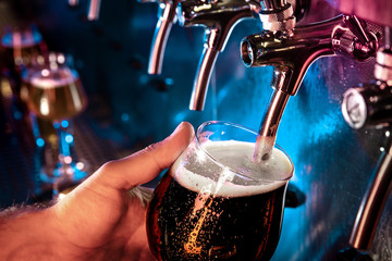 Fototapeta na wymiar Hand of bartender pouring a large ale, porter, stout beer in tap. Bright and modern neon light, males hands. Pouring beer for client. Side view of young bartender pouring beer while standing at the