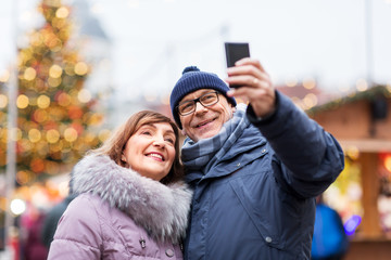 technology, winter holidays and people concept - happy senior couple taking selfie by smartphone at...