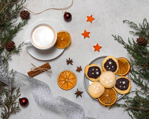 Christmas still life with decorated cookies, a cup of coffee. Light background with fir branches, anise stars, slices of dry orange, cinnamon, Christmas balls.