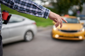 Image of man with outstretched hand stopping taxi in afternoon on blurred background.