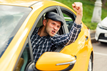 Photo of angry driver in plaid shirt sitting in yellow taxi on summer.