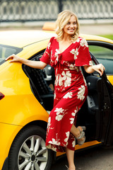 Full-length photo of blonde in red dress standing near taxi on summer.