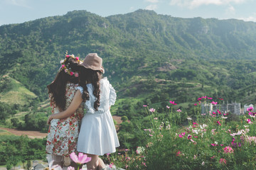 Rear view of couple young woman are  hugging among English garden in vacation morning. Mountain background