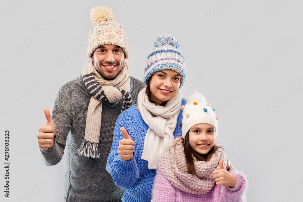 Canvas Prints family, christmas and winter clothes concept - happy mother, father and little daughter in knitted hats and scarves showing thumbs up over grey background