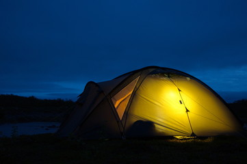 Glowing tent in night tundra on the banks of the river on the Kola Peninsula.