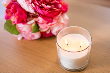Fototapeta na wymiar decoration, hygge and cosiness concept - burning fragrance candle and flower bunch on wooden table