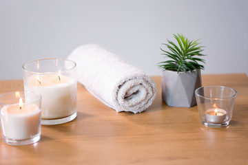 Fototapeta na wymiar decoration, hygge and spa concept - burning white fragrance candles, bath towel and succulent on table
