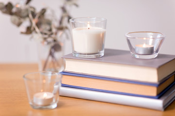 decoration, hygge and cosiness concept - fragrance candles burning in glass holders and books on wooden table