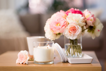 decoration, hygge and cosiness concept - burning fragrance candle and flower bunch on wooden table