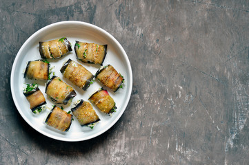 Rolls of fried eggplant plates stuffed with walnuts, cream, garlic, cheese and cilantro greens on a white plate.