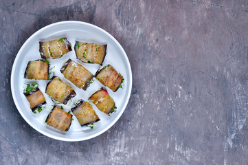 Rolls of fried eggplant plates stuffed with walnuts, cream, garlic, cheese and cilantro greens on a white plate.