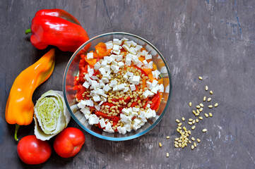 Salad slicing of red and yellow sweet peppers, tomatoes sprinkled with pine nuts and cubes of feta cheese.