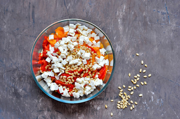 Salad slicing of red and yellow sweet peppers, tomatoes sprinkled with pine nuts and cubes of feta cheese.