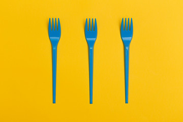 Three blue disposable plastic forks over a yellow background.