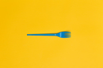 Single blue disposable fork over a yellow background.