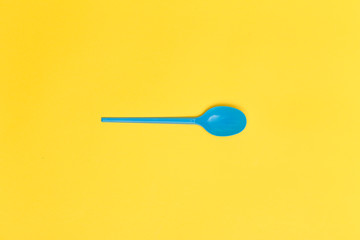 Single blue disposable spoon over a yellow background.