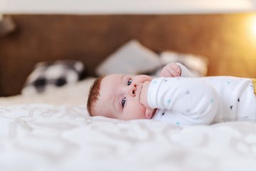 Side view of adorable caucasian baby boy six months old lying in bed and sucking fingers.