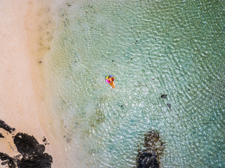 Aerial view of people in summer holiday vacation with beautiful girl on coloured trendy lilo relaxing and sunbathing on clear green ocean lagoon beach water