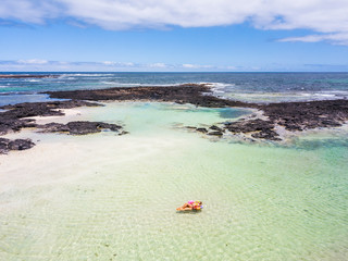 Aerial view of people in summer holiday vacation with beautiful girl on coloured trendy lilo relaxing and sunbathing on clear green ocean lagoon beach water
