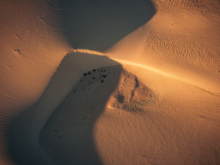 Above view of desert dunes - concept of wild adventure travel destination and beauty of the planet in untouched nature and outdoors - mountains in background and shadows on the sand
