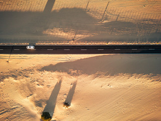 Aerial view of black straight asphalt road with sand and desert on both sides around - car traveling in the middle - concept of wanderlust for exotic and desert destinations