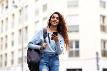 young woman walking in city with bag and cellphone