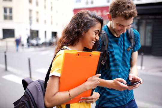 happy college students looking at cellphone in city