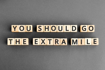You should go the extra mile - phrase from wooden blocks with letters, to make a special effort try harder concept,  grey background