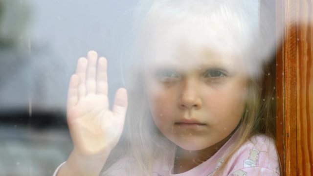 Little girl is sad at the dirty window