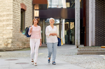 sale, consumerism and people concept - two senior women or friends with shopping bags walking along...