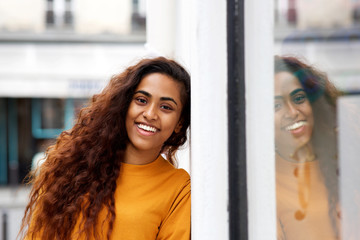 Close up beautiful young indian woman with piercing leaning against wall and smiling