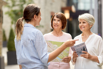 tourism, travel and friendship concept - female passerby showing direction to senior women with city guide and map on tallinn street