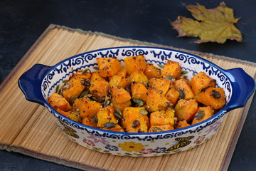 Baked pumpkin slices with garlic and pumpkin seeds in a ceramic form on a dark background, horizontal orientation, closeup
