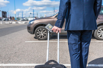 Man in a blue suit with a suitcase and american passport at the airport parking on the backdrop of...