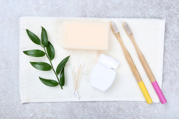 Bamboo toothbrushes with soap, towel, green leafs and dental floss on grey background