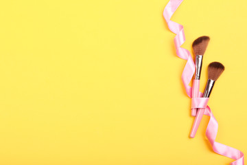 Makeup brushes with ribbon on yellow background