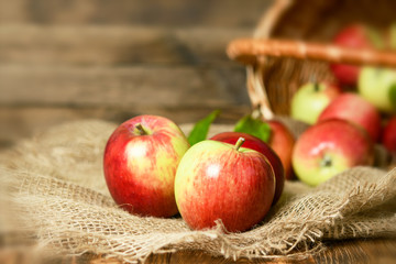 Red organic apples in a wicker basket on a wooden background.