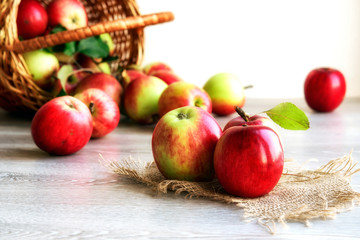 Red organic apples in a wicker basket on a wooden background.