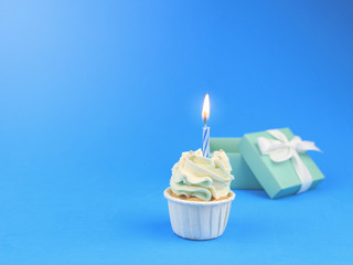 Sweet cupcake with bow candle and gift box on blue background with copy space. Happy birthday party background concept. 