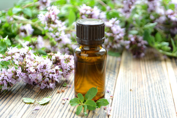 Essential oil of oregano in a bottle and fresh flowers on a wooden table Natural cosmetics and aromatherapy