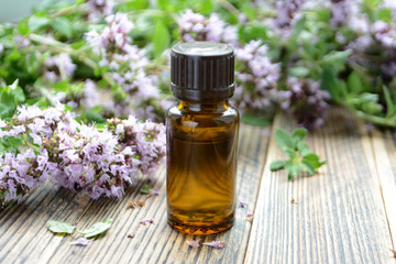 Essential oil of oregano in a bottle and fresh flowers on a wooden table Natural cosmetics and aromatherapy