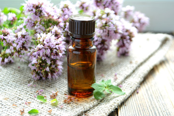 Essential oil of oregano in a bottle and fresh flowers on a wooden table Natural cosmetics and aromatherapy