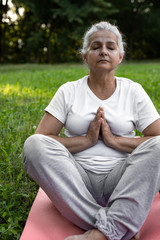 Beautiful senior woman is meditating in the park