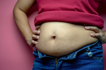 Overweight fat woman touching obese belly isolated on a pink background in Studio, closeup. Weight losing, obesity, cellulite, health care concept.