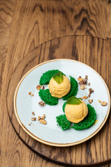 Close up of couple of scoops of frozen mango sorbet with nuts and green biscuit, served on wooden table