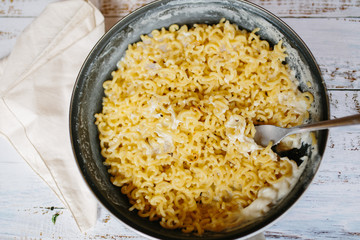 Classic Homemade Macaroni and Cheddar Cheese on black plate with a fork on white wooden table. Top view