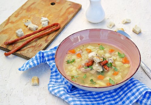 Yellow pea soup with potatoes, carrots, ham and smoked sausages in a clay bowl on a light concrete background. Served with white bread croutons.