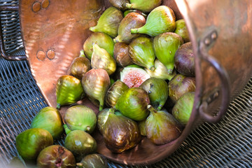 Harvesting figs in a metallic copper kitchenware on a wicker surface in sunlight. Rustic Provence.